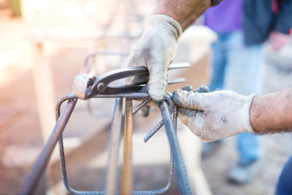 worker using pincers and steel wire to secure bars for concrete